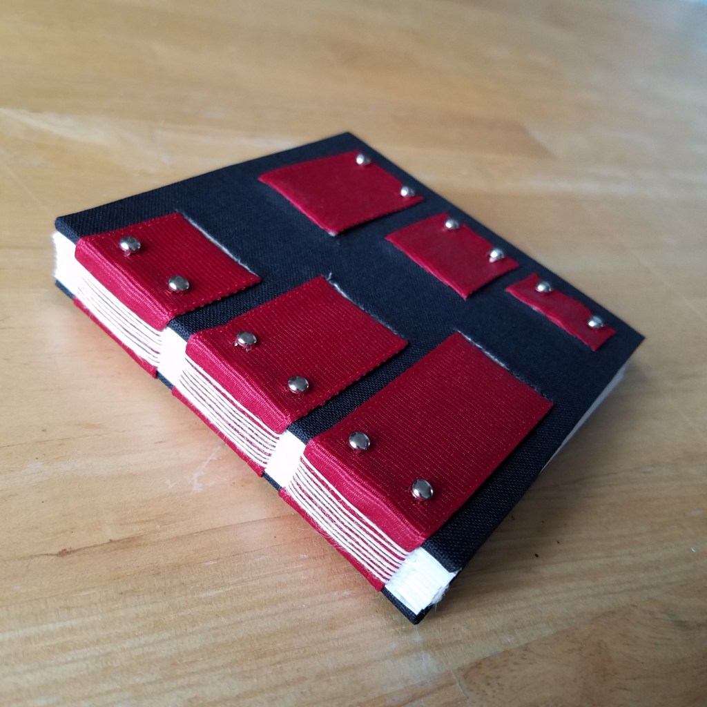 Ribbon book sits closed, showing white thread clearly against red thread.